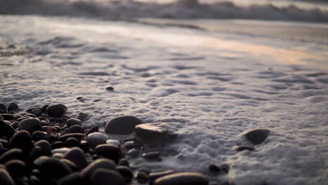 Close-up-beach-waves-and-foam-bubbling-through-pebbles-and-rocks-slowmo