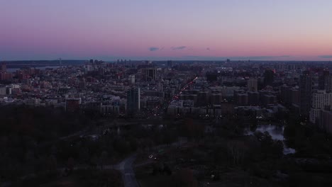 Drone-flyover-the-top-of-New-York-City's-Central-Park-with-the-Harlem-Meer-in-view-and-the-Harlem-neighborhood-in-the-distance,-at-Sunrise-Blue-Hour,-in-4K