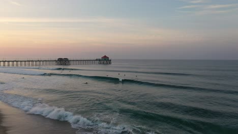 In-4k-a-surfer-catches-a-wave-at-sunrise-in-Surf-City-California-USA-with-the-pier-beautifully-displayed-in-the-background