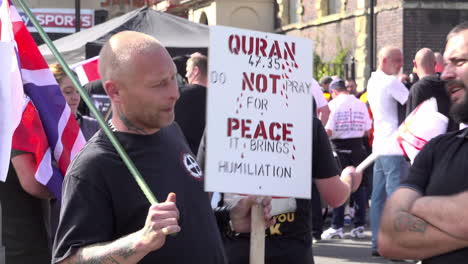 UK-September-2018---A-far-right-tattooed-skinhead-with-a-Celtic-cross-white-supremacy-symbol-on-his-T-shirt-stands-holding-an-anti-muslim-placard-and-a-British-Union-flag