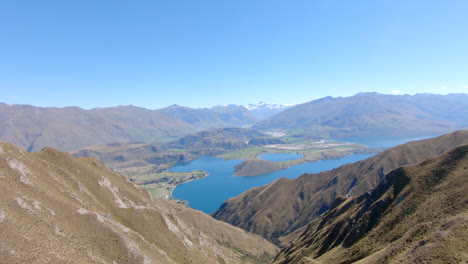 Wide-scenic-view-from-the-top-of-Roys-Peak-onto-Lake-Wanaka-and-the-mountains-of-Mount-Aspiring-National-Park,-panning-from-right-to-left
