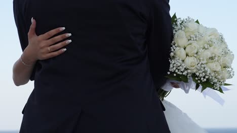 Close-up-of-a-bride-and-groom-embracing-as-the-wind-gently-blows-her-bouquet,-no-faces