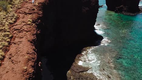 Drone-shots-of-a-cliff-side-beach-with-blue-waters-and-no-one-around-but-1-man-running-on-the-cliffs-edge