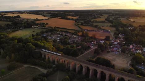 A-train-moving-across-a-viaduct-in-Chapel,-Essex-at-Sunset