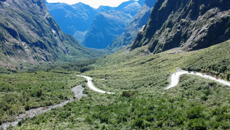 Toma-Aérea-De-Un-Valle-En-El-Parque-Nacional-De-Fiordland-Con-Autos-Conduciendo-En-Un-Camino-Sinuoso-En-Un-Día-Soleado