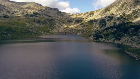 Wide-aerial-drone-slowly-flying-over-a-lake-towards-a-mountain-range