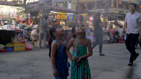 Young-asian-girls-stand-under-sprinkler-and-smile---On-the-street-in-Vietnam