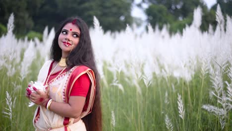 A-beautiful-and-religious-married-Indian-woman-holding-a-shankha-or-conch-shell-looks-behind-in-a-field-of-white-flowered-grass-or-kaash-phool