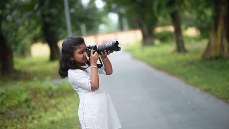 A-cute-little-Asian-girl-is-taking-photos-of-nature-and-trees-in-a-jungle-with-a-Digital-SLR-camera-like-a-Professional-photographer