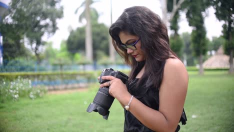 A-tourist-Asian-girl-takes-photos-with-a-DSLR-camera-and-checks-the-photos-in-camera-display-at-a-nature-park