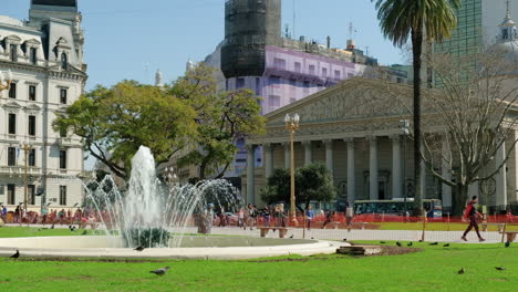 Fountain-and-people-walking-in-May-Square,-Buenos-Aires-Cathedral-in-background-at-daytime-wide-shot