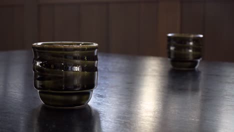 Pan-up-over-two-Japanese-cups-on-a-table-inside-a-restaurant-setting-with-outside-window-reflections-on-surface