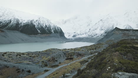 A-panning-shot-of-a-glacial-lake-surrounded-by-snow-capped-mountains-on-a-cold-winters-day-in-New-Zealand