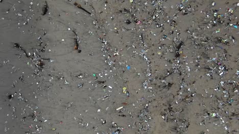 Pulling-back-aerial-shot-of-an-ecological-disaster,-plastic-waste-on-the-beach-dying-planet