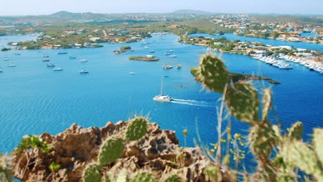 Yacht-sailing-out-of-bright-blue-Caribbean-sea-marina,-Pan-from-above