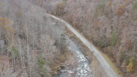 Drone-shot-of-river-and-road-looking-downstream-rising-altitude-in-late-fall-in-western-North-Carolina