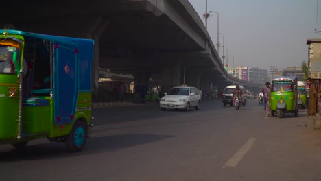 Traffic-close-up-at-the-road-under-the-fly-over,-passing-motor-bikes-and-cars,-cycle,-Buses,-rickshaw`s,-Billboards-and-buildings-in-the-background