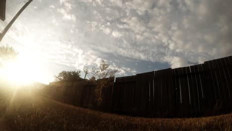 TIME-LAPSE---Sun-glaring-through-a-wooden-fence-in-a-back-yard-on-a-sunny-day-well-the-clouds-fly-over