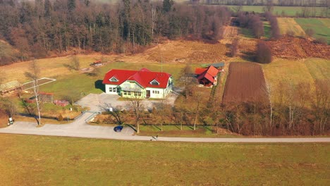 Aerial-shot-arcing-around-a-farmhouse-while-a-person-walks-a-dog-along-the-road