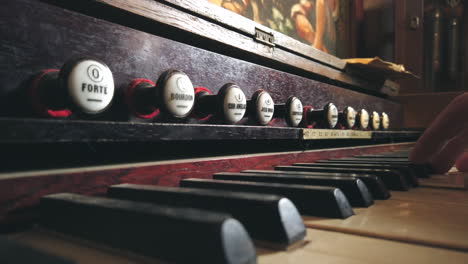 Close-up-of-an-open,-unfolded-harmonium-as-a-hand-reaches-in-to-pull-the-stop-levers
