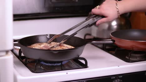 A-side-view-of-three-pieces-of-filled-chicken-breast-frying-in-a-forged-frying-pan-on-top-of-a-gas-stove