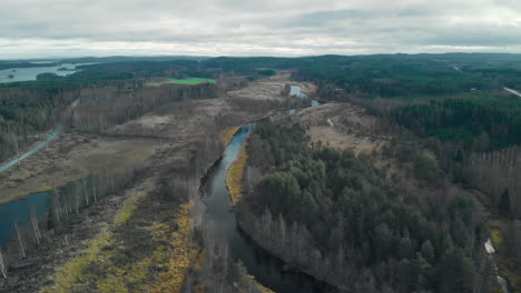Aerial,-drone-shot,-flying-over-a-river-surrounded-by-leafless-autumn-forest,-on-a-cloudy-fall-day,-in-Juuka,-Pohjois-Karjala,-Finland