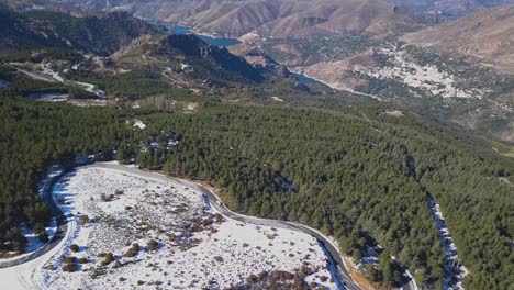 Aerial-view-of-road-in-the-snowed-mountains-and-a-car-driving-through-that-road