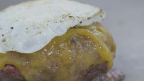 Macro-close-up-of-a-cheeseburger-patty-on-a-restaurant-grill-with-a-fried-egg-on-top-as-it-cooks