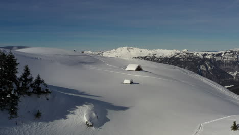 Luftaufnahme,-Die-Im-Winter-Zu-Einer-Schneebedeckten-Berghütte-In-Den-Französischen-Alpen-Fliegt,-Bevor-Sie-über-Den-Rand-Des-Hügels-Fliegt-Und-Das-Tal-Und-Die-Berge-Enthüllt