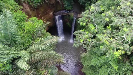 Waterfall-with-pond-hidden-in-the-jungle-among-palm-trees,-drone-shot-flying-up-throught-palm-trees