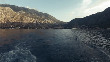 Static-POV-shot,-from-a-boat-leaving-Kotor-city,-surrounded-by-mountains,-boats-on-the-adriatic-sea,-on-a-sunny-day,-in-Montenegro