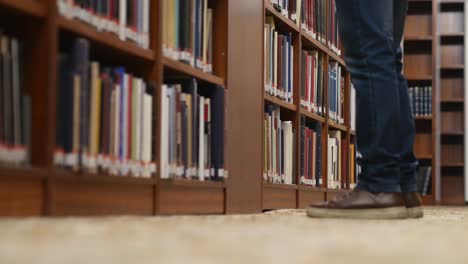 Low-angle-shot-of-a-person's-legs-walking-as-they-stop-to-look-for-a-book-in-the-library