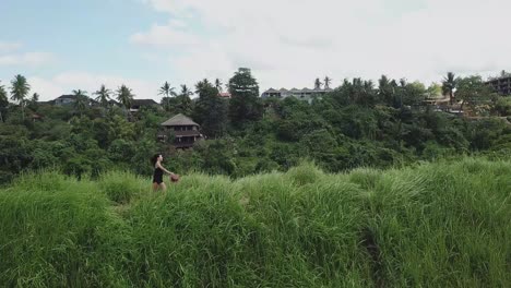 Zeitlupenaufnahmen-Eines-Schönen-Mädchens,-Das-Den-Weg-In-Einem-Reisfeld-Auf-Einem-Hintergrund-Aus-Palmendschungel-Hinunterläuft