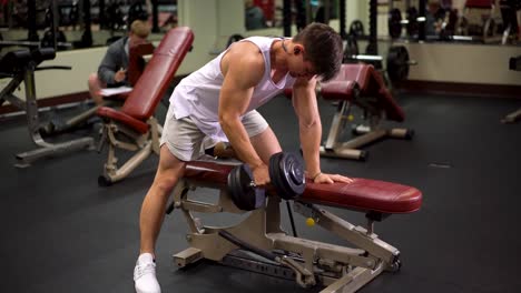 Front-side-shot-of-young-bodybuilder-doing-one-arm-dumbbell-rows-using-a-bench