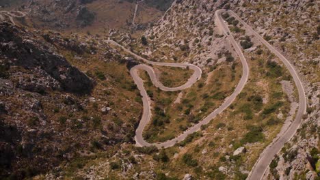 AERIAL:-Tilt-up-from-serpentine-road-to-panoramic-mountain-view-in-spain