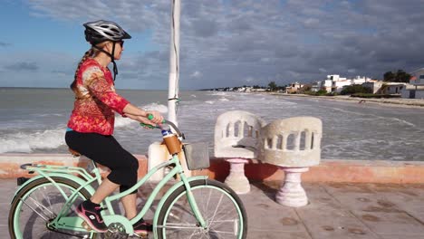 Closeup-of-mature-woman-riding-cruiser-bicycle-on-a-pier-with-a-sea-in-the-background