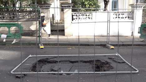 UK-February-2019---People-walk-past-a-fenced-off-sink-hole-that-has-opened-up-in-the-road-in-London’s-affluent-area-of-Kensington