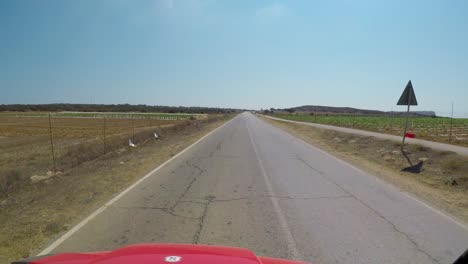 Point-of-view-driving-on-paved-road-past-farmland-in-Cyprus-and-a-small-roadside-fruit-stand