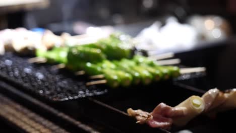 Close-up-of-yakitori,-grilled-skewered-chicken,-being-cooked-alongside-green-peppers