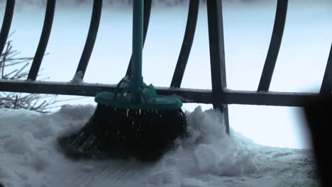A-close-up-of-a-broom-pushing-out-snow-from-a-balcony