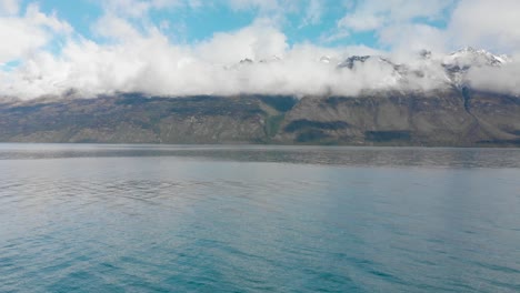 Cámara-Lenta---Volando-Sobre-El-Hermoso-Lago-Azul-Wakatipu,-Queenstown,-Nueva-Zelanda-Con-Montañas,-Nieve-Fresca-Y-Nubes-Cielo-Azul-En-El-Fondo---Drone-Aéreo