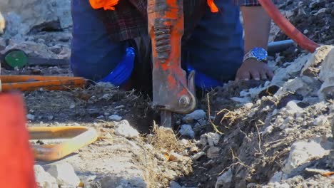 Man-clearing-debris-by-hand-in-trench-by-his-jack-hammer-close-up-camera-zooming-out