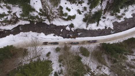 Top-down-drone-shot-of-three-horse-teams-riding-a-narrow-mountain-valley-next-to-a-stream