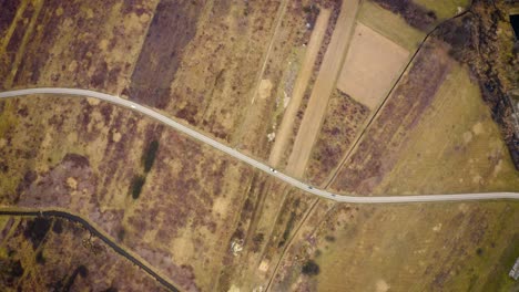 Aerial-view-high-above-car-driving-through-dry-farm-land-road-trip-flying-over-car-on-empty-country-road-in-barren-landscape-4k-footage-of-cars-on-road