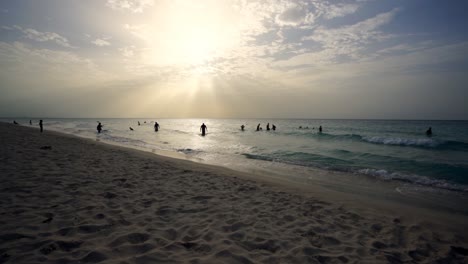 Cuba-beach-in-Varadero-during-sunset,-the-beach-is-crowded-with-people-swimming-in-the-sea,-backlit,silhouette