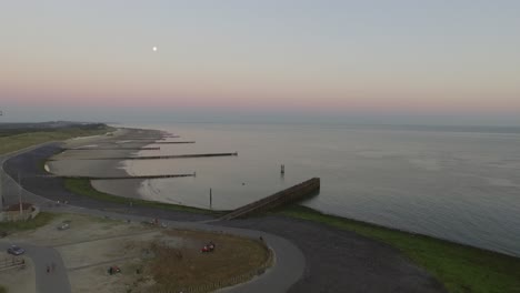 Aerial:-The-pier,-beach-and-lighthouse-during-sunset-near-the-village-Westkapelle,-the-Netherlands