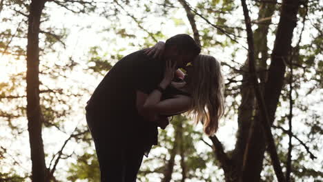 Young-couple-kissing-each-other-and-laughing-during-sunset-in-a-forest