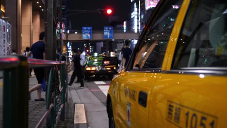 Tokyo-taxi-at-night,-with-the-reflection-of-the-taxi-sign-shot-in-the-taxi’s-wing-mirror-and-passers-by-in-the-background
