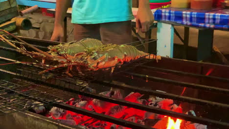 A-close-up-shot-of-2-lobsters-while-on-the-barbecue-with-flame,-metal-grill-on-person-unrecognisable-in-the-background