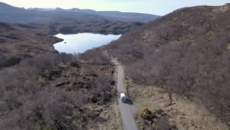 Aerial-footage-of-a-vintage-VW-campervan-driving-down-a-country-road-on-a-sunny-day-in-Assynt,-Scottish-Highlands,-Scotland